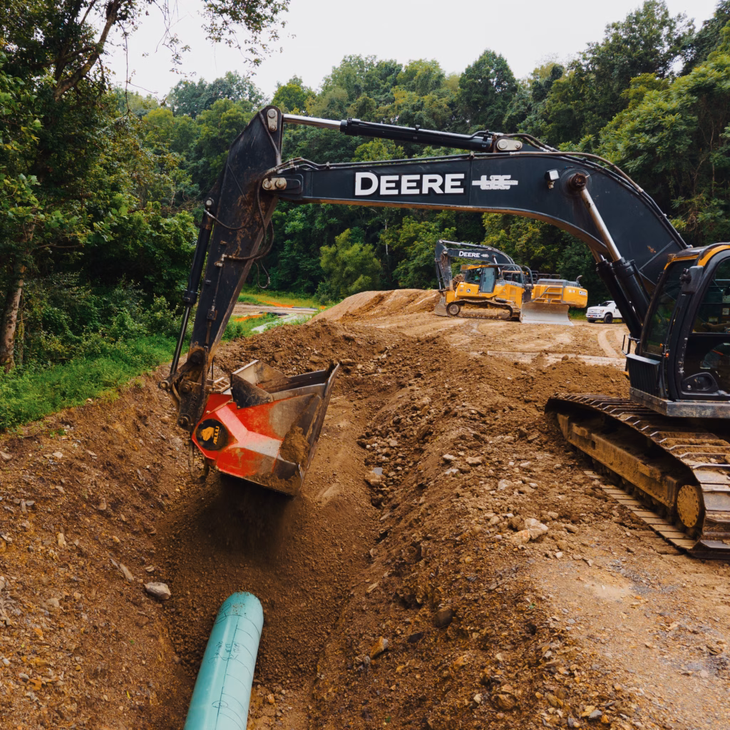 The ALLU screening bucket padding a pipeline ditch with machinery in the background.